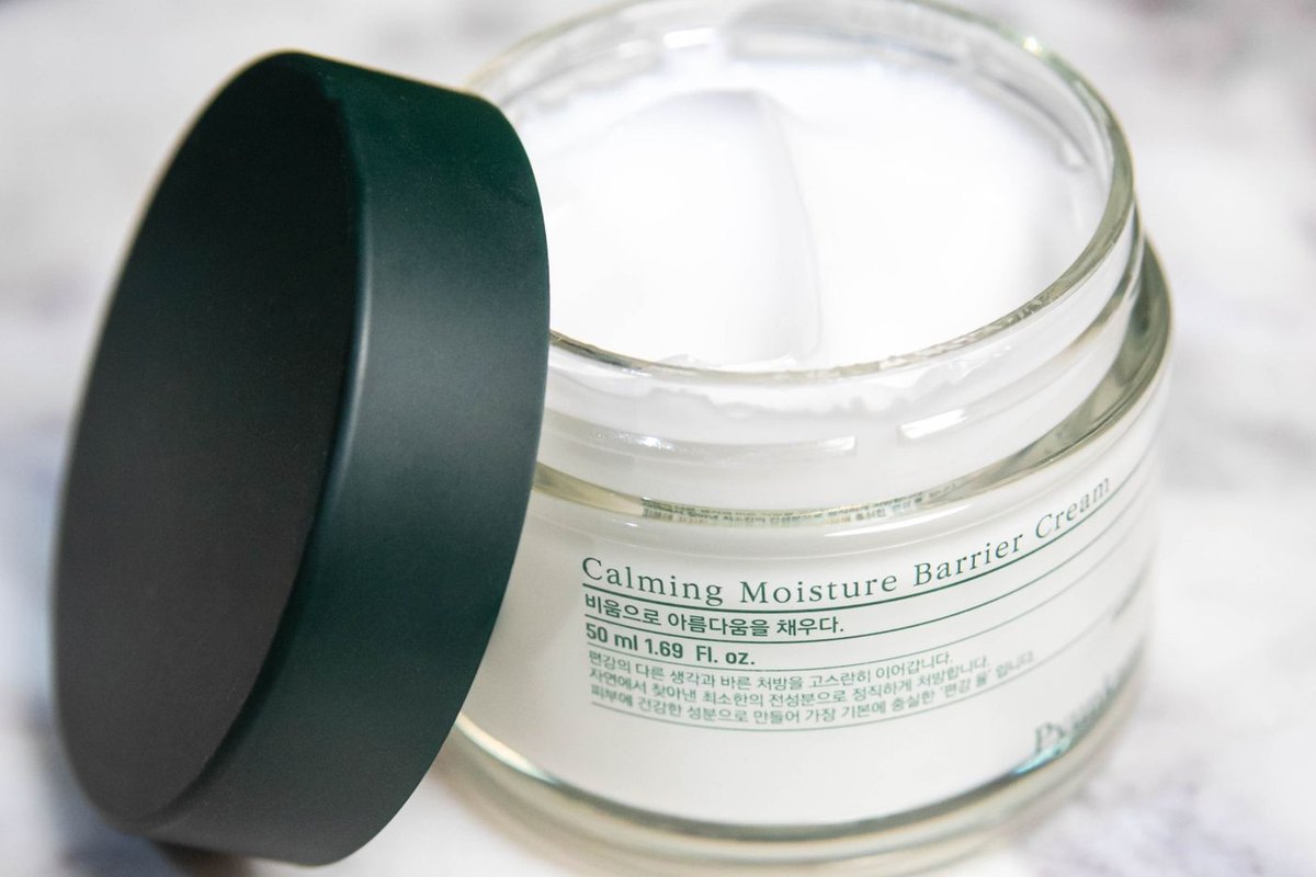 A close-up of an open glass cosmetics jar with its dark lid resting beside it