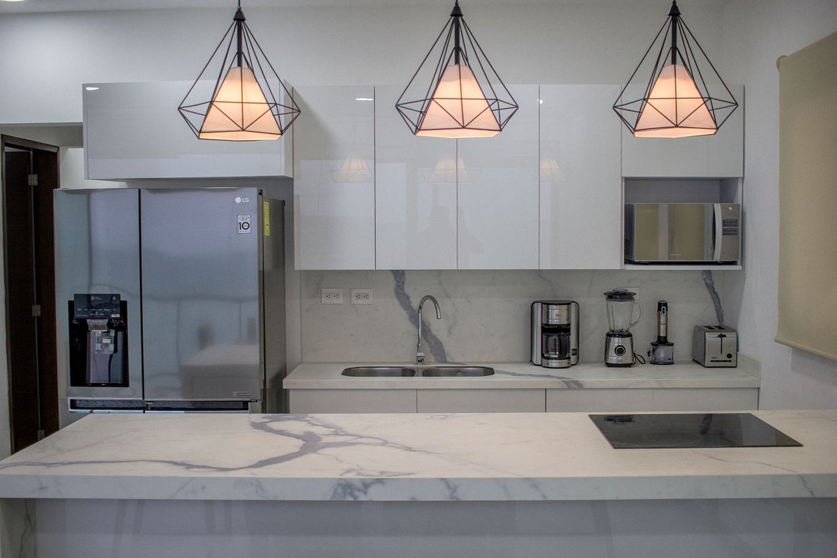 A kitchen with a marble island, three pendant lamps and a run of white units