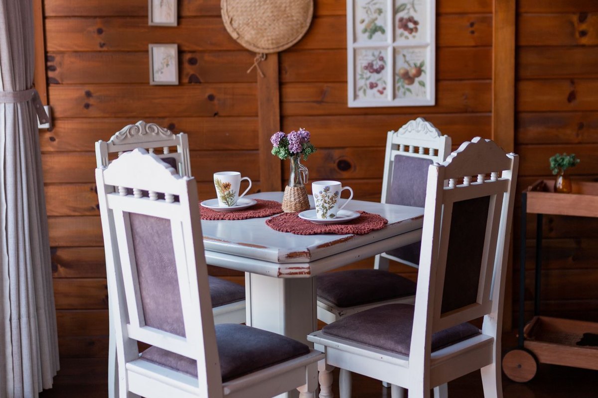 A white dining table set with two cups and a small vase of flowers in a wood-panelled room