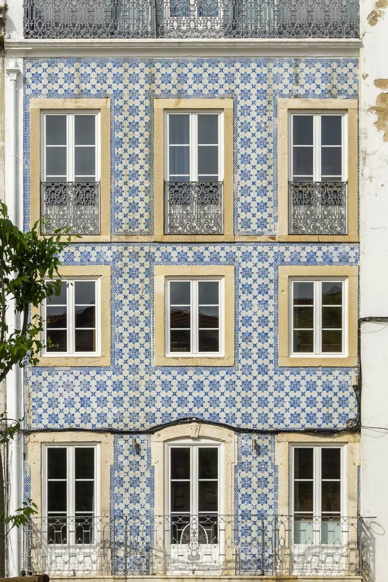 A vertical photo of a tiled Lisbon facade, three rows of windows with iron balconies