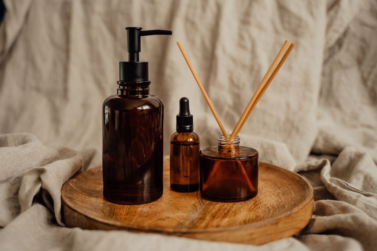 Three amber glass bottles and a reed diffuser on a round wooden tray, wrapped in crumpled linen