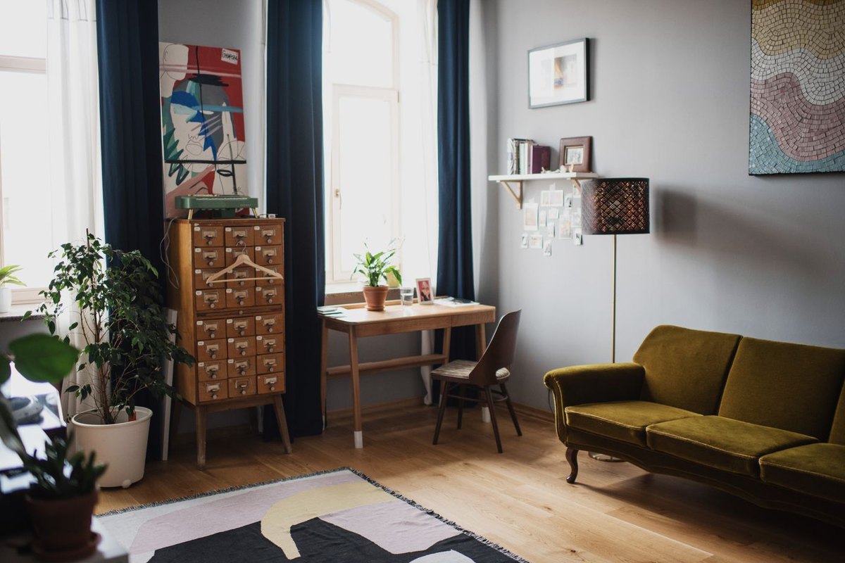 A living room with navy curtains, an olive velvet sofa, a wooden card cabinet and a bold abstract canvas