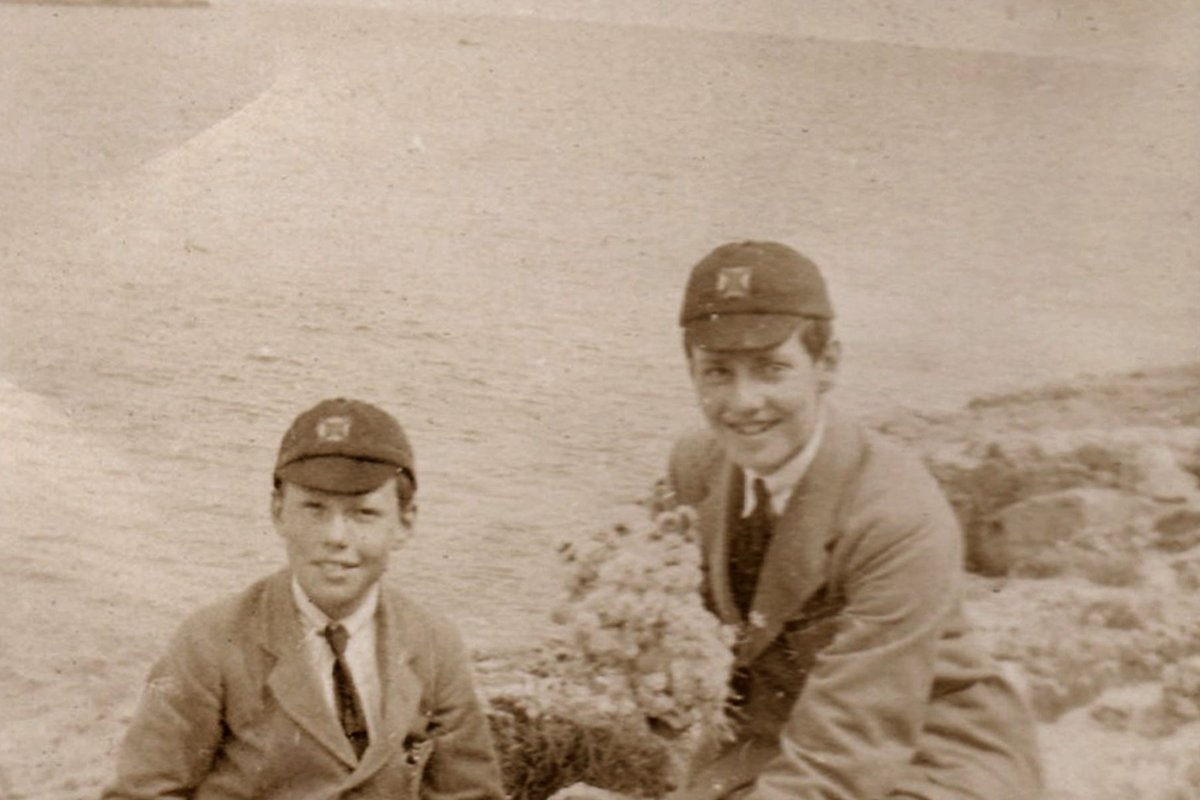 A faded sepia photograph of two boys sitting by the sea