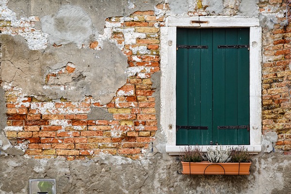 A small, soft photo of a weathered brick wall with a green shuttered window and a flower box