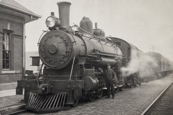 A small, faded black and white scan of a steam locomotive and railway worker